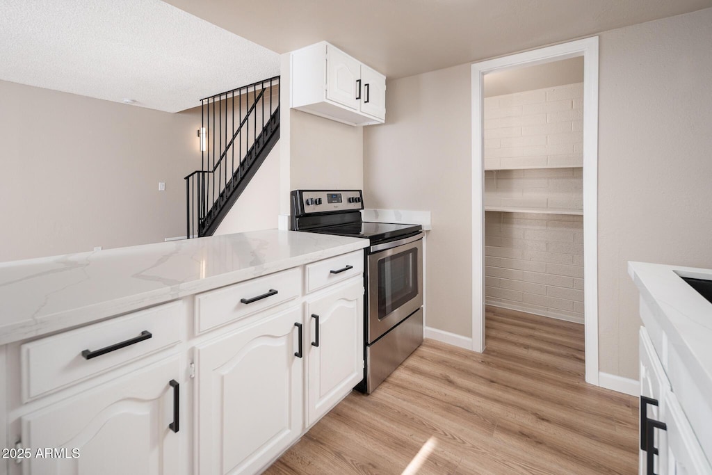 kitchen featuring stainless steel electric range, white cabinets, light stone countertops, a textured ceiling, and light hardwood / wood-style flooring