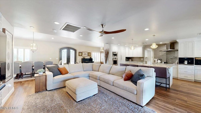 living room featuring ceiling fan with notable chandelier, french doors, and light wood-type flooring