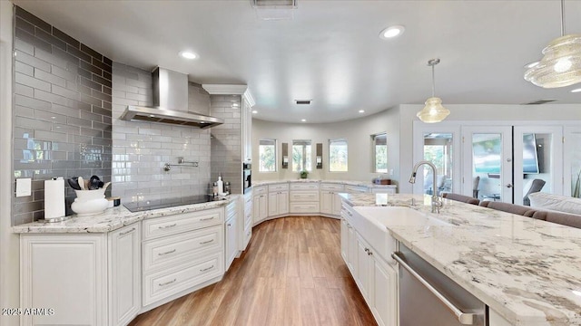 kitchen with stainless steel appliances, sink, wall chimney range hood, and decorative light fixtures