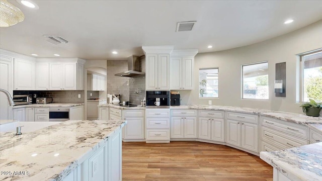 kitchen with white cabinetry, a healthy amount of sunlight, wall chimney exhaust hood, and black appliances