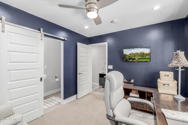 office featuring a barn door, a ceiling fan, light colored carpet, baseboards, and a textured wall