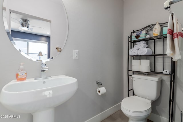 half bathroom with baseboards, toilet, a sink, and ceiling fan