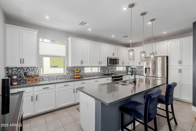 kitchen with a sink, appliances with stainless steel finishes, light tile patterned floors, white cabinetry, and a breakfast bar