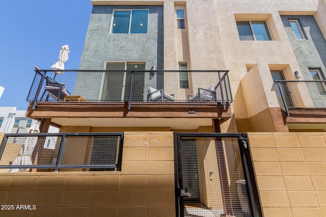 back of property featuring a balcony, a gate, stucco siding, and fence