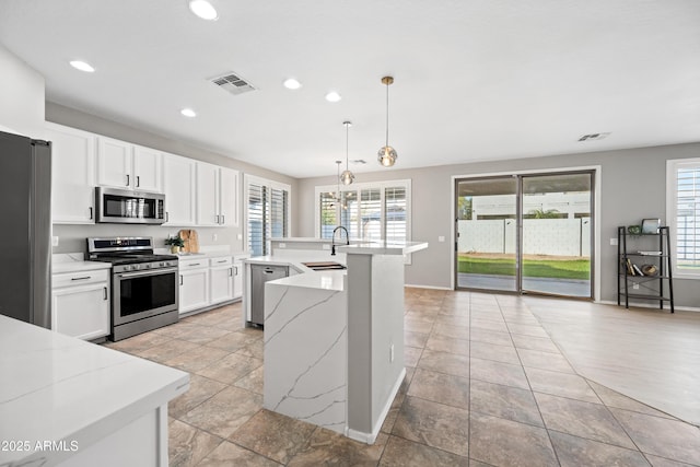 kitchen with sink, appliances with stainless steel finishes, an island with sink, white cabinets, and decorative light fixtures