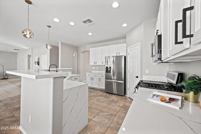 kitchen with appliances with stainless steel finishes, pendant lighting, white cabinetry, an island with sink, and light stone countertops