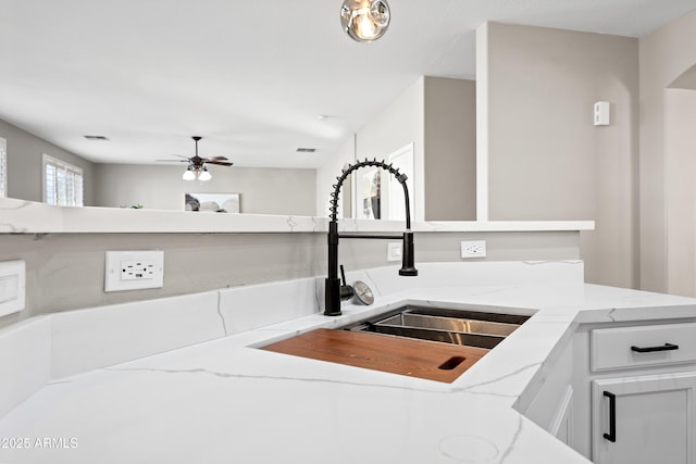 kitchen with light stone counters, sink, white cabinets, and ceiling fan