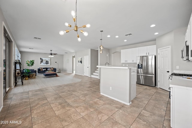 kitchen featuring white cabinetry, decorative light fixtures, a center island with sink, appliances with stainless steel finishes, and ceiling fan with notable chandelier