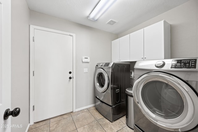 laundry area featuring cabinets, washing machine and dryer, light tile patterned floors, and a textured ceiling