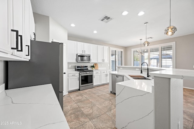 kitchen featuring sink, light stone counters, hanging light fixtures, stainless steel appliances, and white cabinets