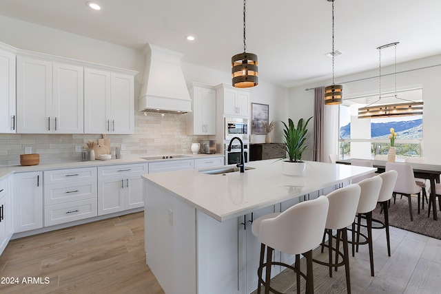 kitchen with pendant lighting, custom exhaust hood, stainless steel microwave, and sink