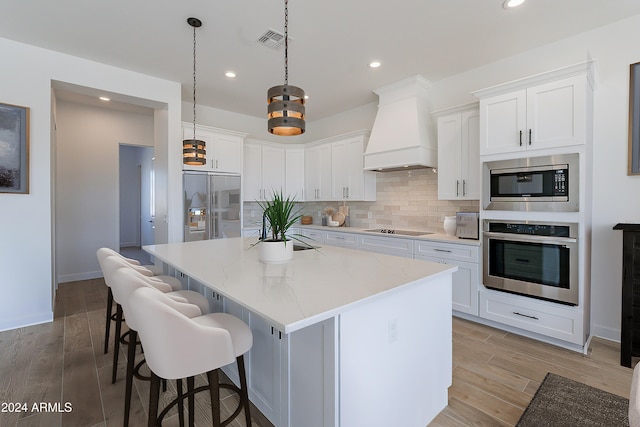 kitchen featuring white cabinetry, a center island, stainless steel appliances, pendant lighting, and custom exhaust hood