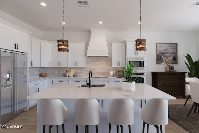 kitchen with sink, built in appliances, pendant lighting, white cabinets, and custom exhaust hood