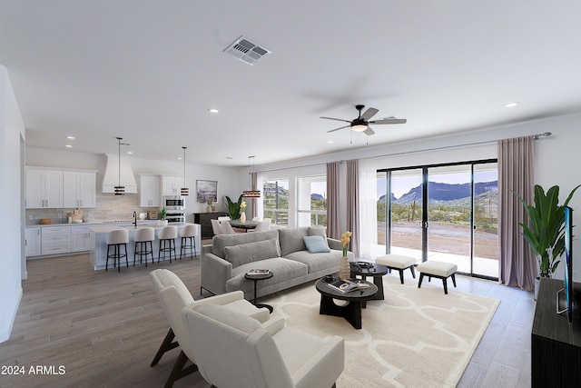 living room featuring a mountain view, light hardwood / wood-style floors, ceiling fan, and sink