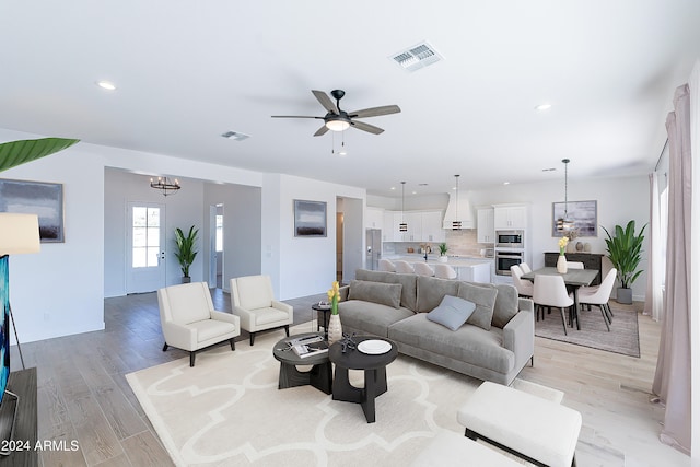 living room with ceiling fan with notable chandelier and light hardwood / wood-style flooring