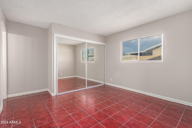 unfurnished bedroom featuring dark tile patterned flooring, a closet, and a textured ceiling