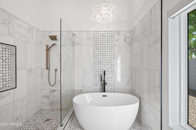full bathroom with tile walls, a walk in shower, a freestanding tub, and a notable chandelier