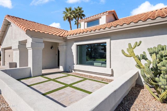 exterior space featuring an attached garage, a patio, stucco siding, and a tile roof
