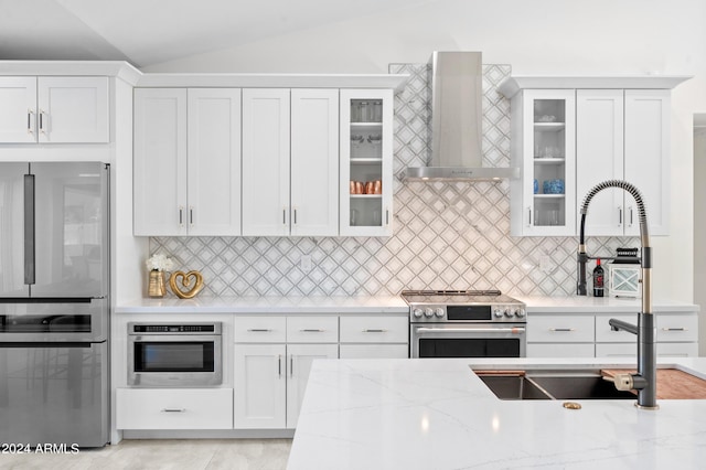 kitchen featuring wall chimney range hood, white cabinets, vaulted ceiling, and appliances with stainless steel finishes