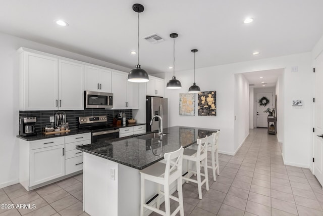 kitchen with visible vents, an island with sink, a sink, stainless steel appliances, and backsplash