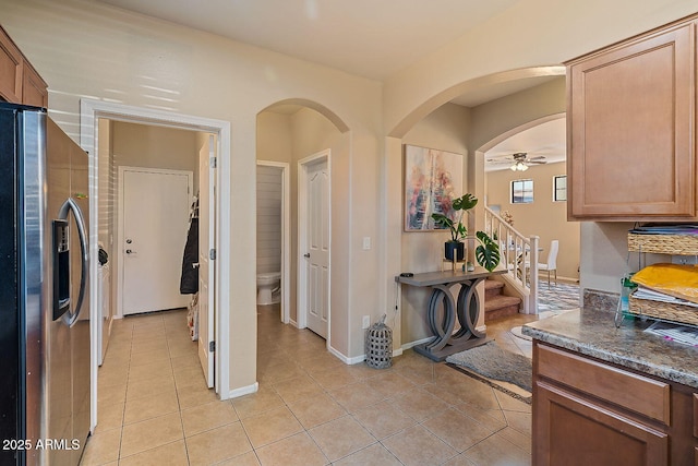 kitchen with dark stone countertops, light tile patterned floors, stainless steel fridge, and ceiling fan