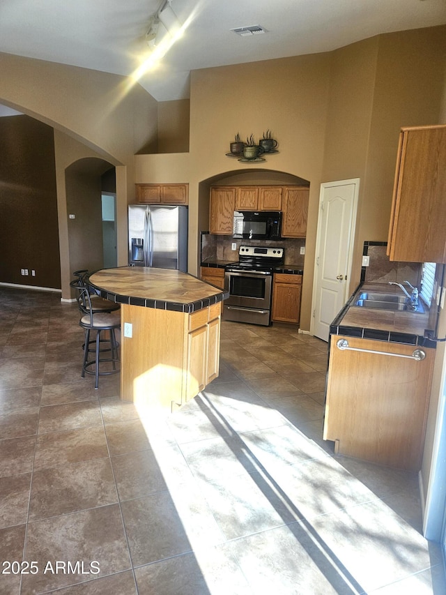 kitchen featuring sink, appliances with stainless steel finishes, tile counters, a kitchen island, and backsplash