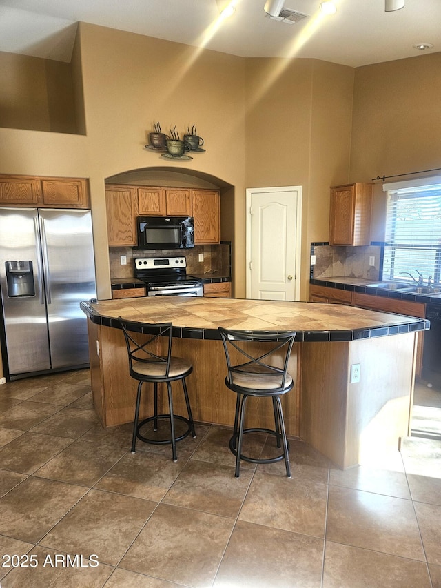 kitchen featuring stainless steel appliances, tile counters, a kitchen bar, and a kitchen island