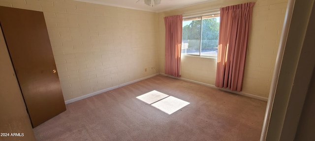 carpeted spare room featuring ceiling fan, ornamental molding, and brick wall