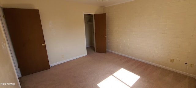 unfurnished bedroom featuring light carpet, a closet, and brick wall