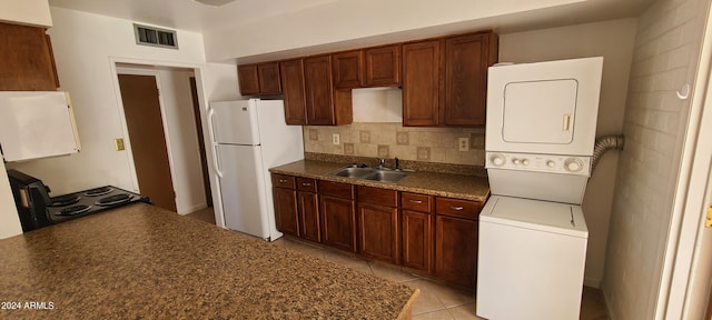 kitchen with black range oven, sink, light tile patterned floors, white fridge, and stacked washer / drying machine