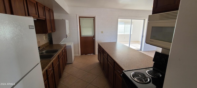 kitchen with sink, white refrigerator, range, washer / dryer, and light tile patterned flooring