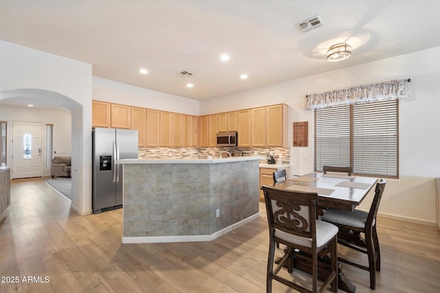 kitchen with stainless steel appliances, a kitchen island, light brown cabinetry, decorative backsplash, and light wood-type flooring