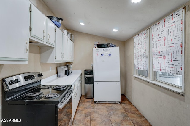 kitchen with stainless steel electric range oven, vaulted ceiling, white cabinets, and white fridge