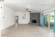 unfurnished living room with ceiling fan, a large fireplace, and wood-type flooring