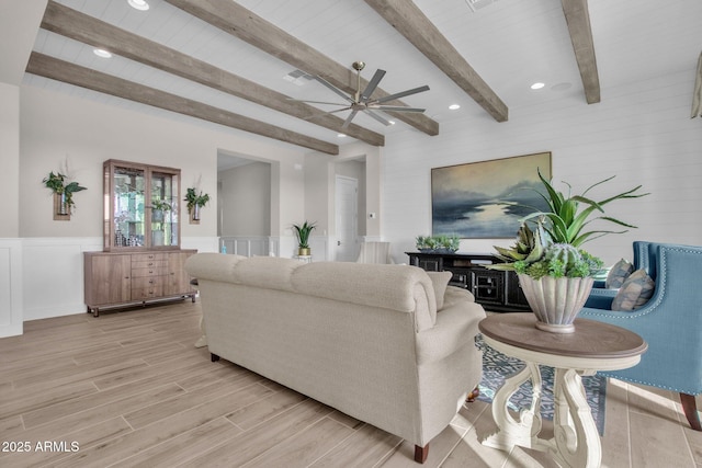 living area featuring beamed ceiling, recessed lighting, a wainscoted wall, a ceiling fan, and light wood-style flooring