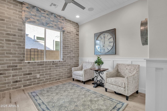 living area featuring visible vents, crown molding, wood finished floors, a wainscoted wall, and a ceiling fan