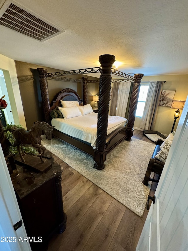 bedroom with wood finished floors, visible vents, and a textured ceiling