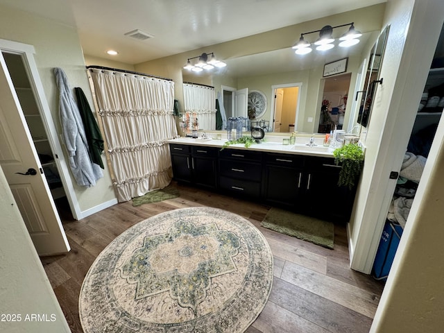 bathroom featuring a sink, double vanity, visible vents, baseboards, and wood finished floors