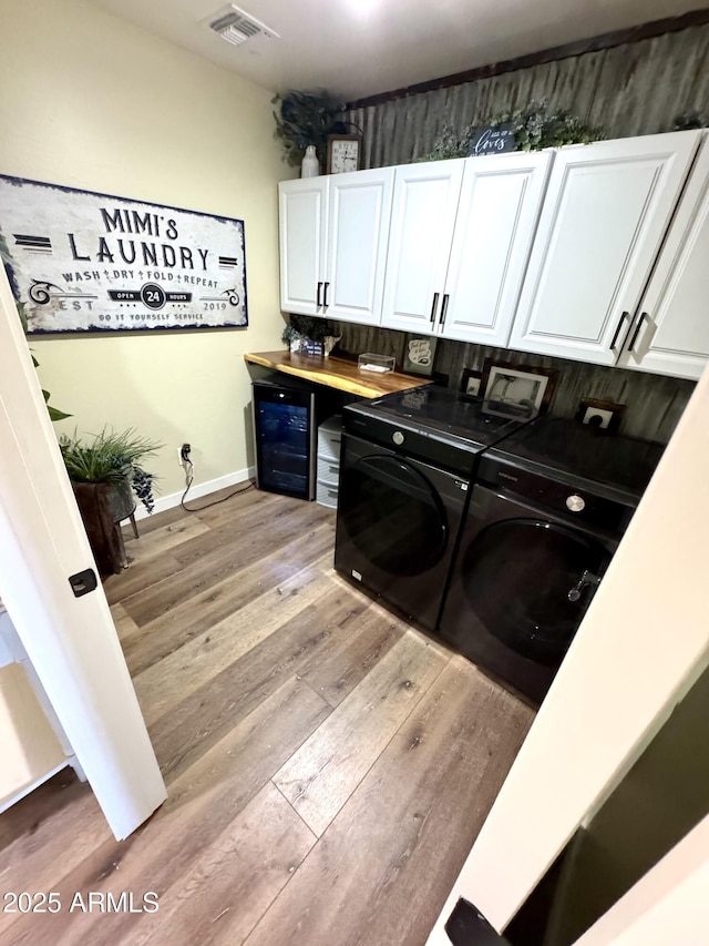 laundry room with washing machine and clothes dryer, beverage cooler, visible vents, light wood-type flooring, and cabinet space