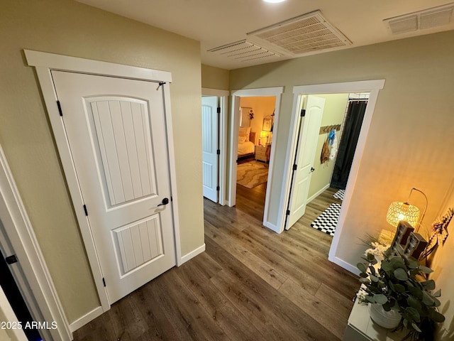 hallway with wood finished floors, visible vents, and baseboards