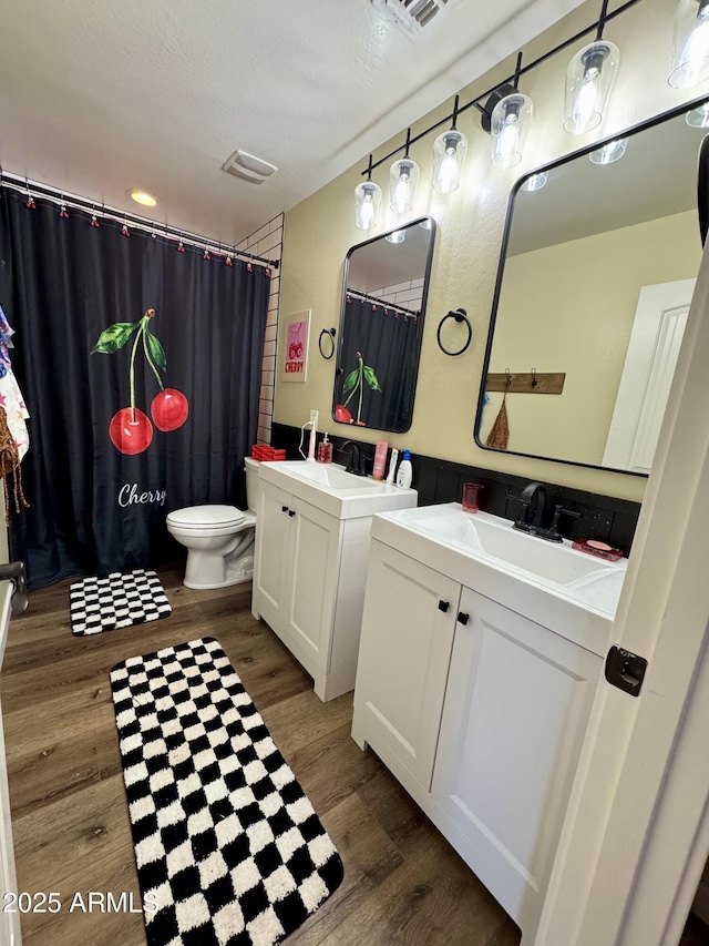 full bath with a sink, visible vents, two vanities, toilet, and wood finished floors
