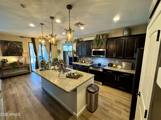 kitchen with an inviting chandelier, light stone counters, stainless steel appliances, a sink, and visible vents