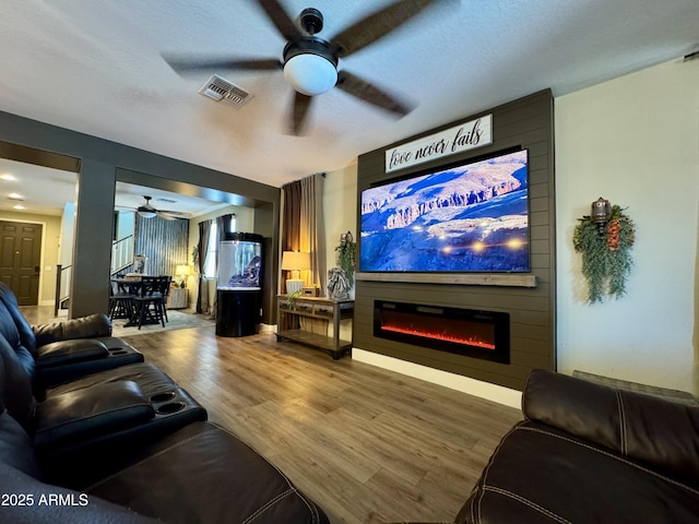 home theater with visible vents, wood finished floors, ceiling fan, and a fireplace