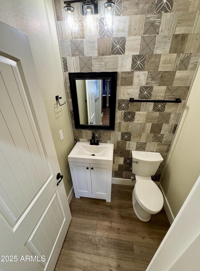 half bathroom with wood finished floors, toilet, vanity, and baseboards