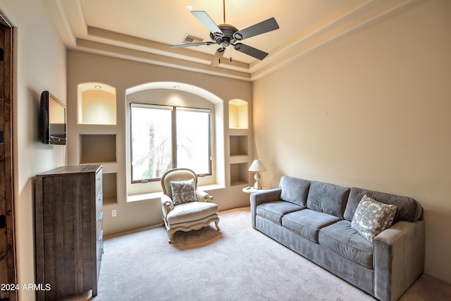 carpeted living room featuring a tray ceiling, built in shelves, and ceiling fan