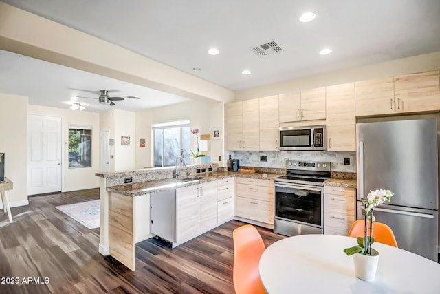 kitchen featuring dark wood-type flooring, sink, stone countertops, appliances with stainless steel finishes, and kitchen peninsula