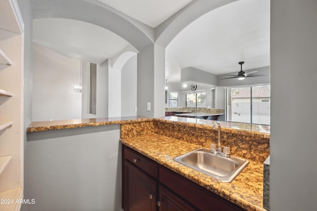 kitchen featuring ceiling fan, dark brown cabinets, light stone countertops, and sink