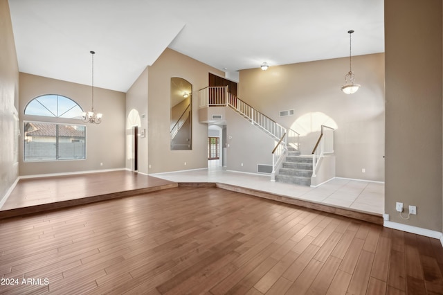 unfurnished living room featuring a notable chandelier, high vaulted ceiling, and light hardwood / wood-style flooring