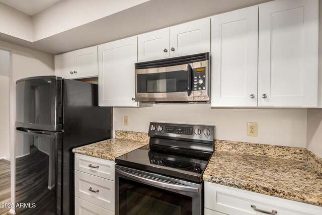 kitchen featuring stainless steel appliances, white cabinetry, light stone counters, and wood finished floors