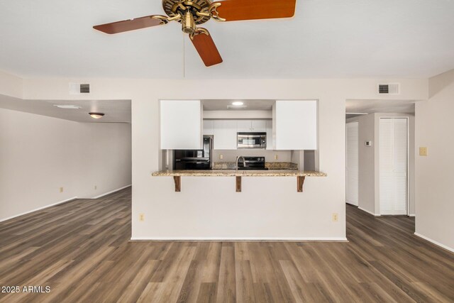 kitchen featuring stainless steel appliances, white cabinets, a kitchen bar, and dark wood-type flooring